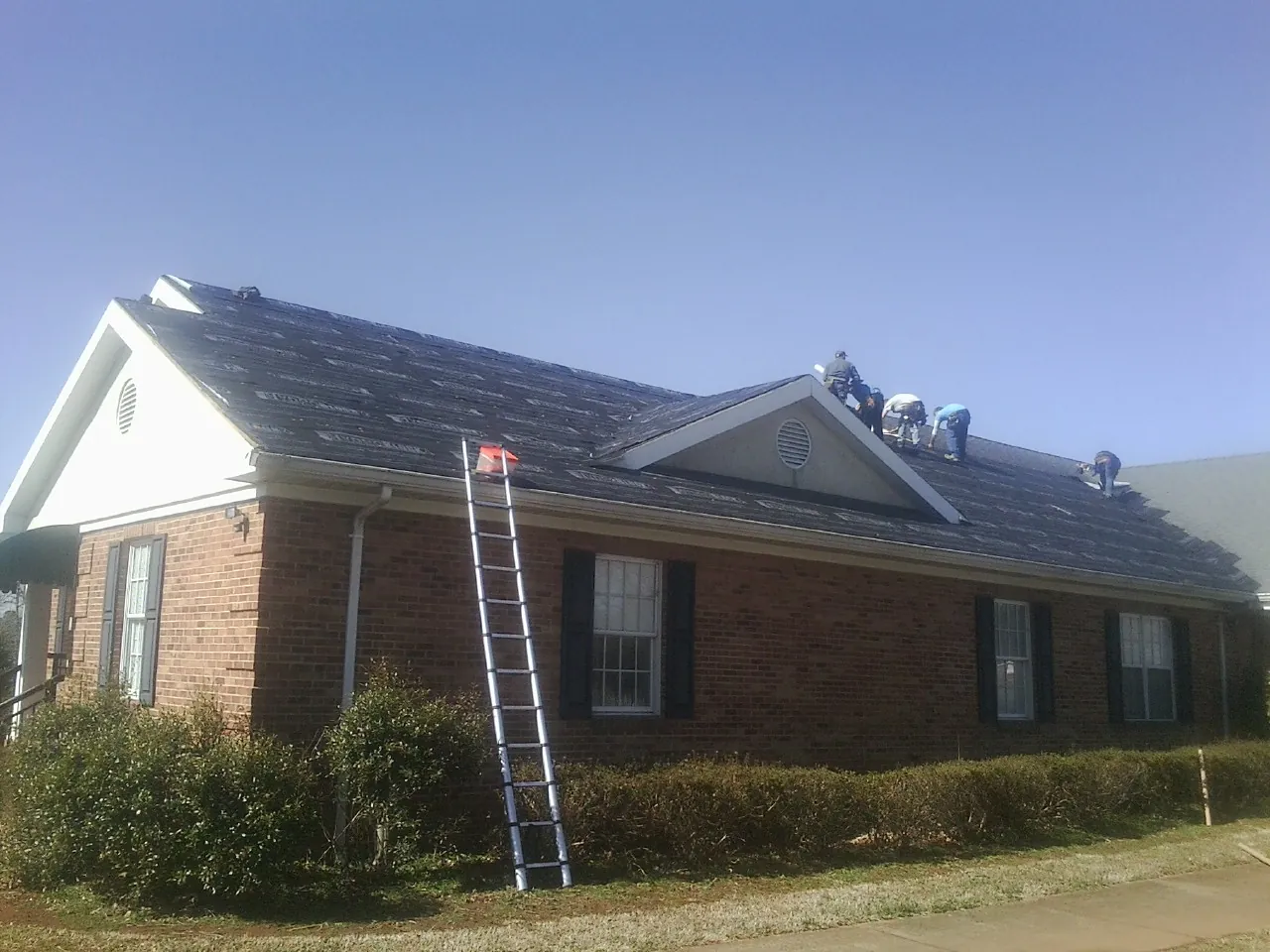 Crew tearing shingles off a brick ranch roof with a ladder set — Emergency Roof Repair work by our crew in Luray