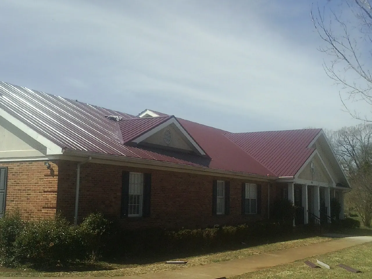 Red metal roof with gabled entries on a long brick building, from a Hail Damage Roof Repair job in Luray