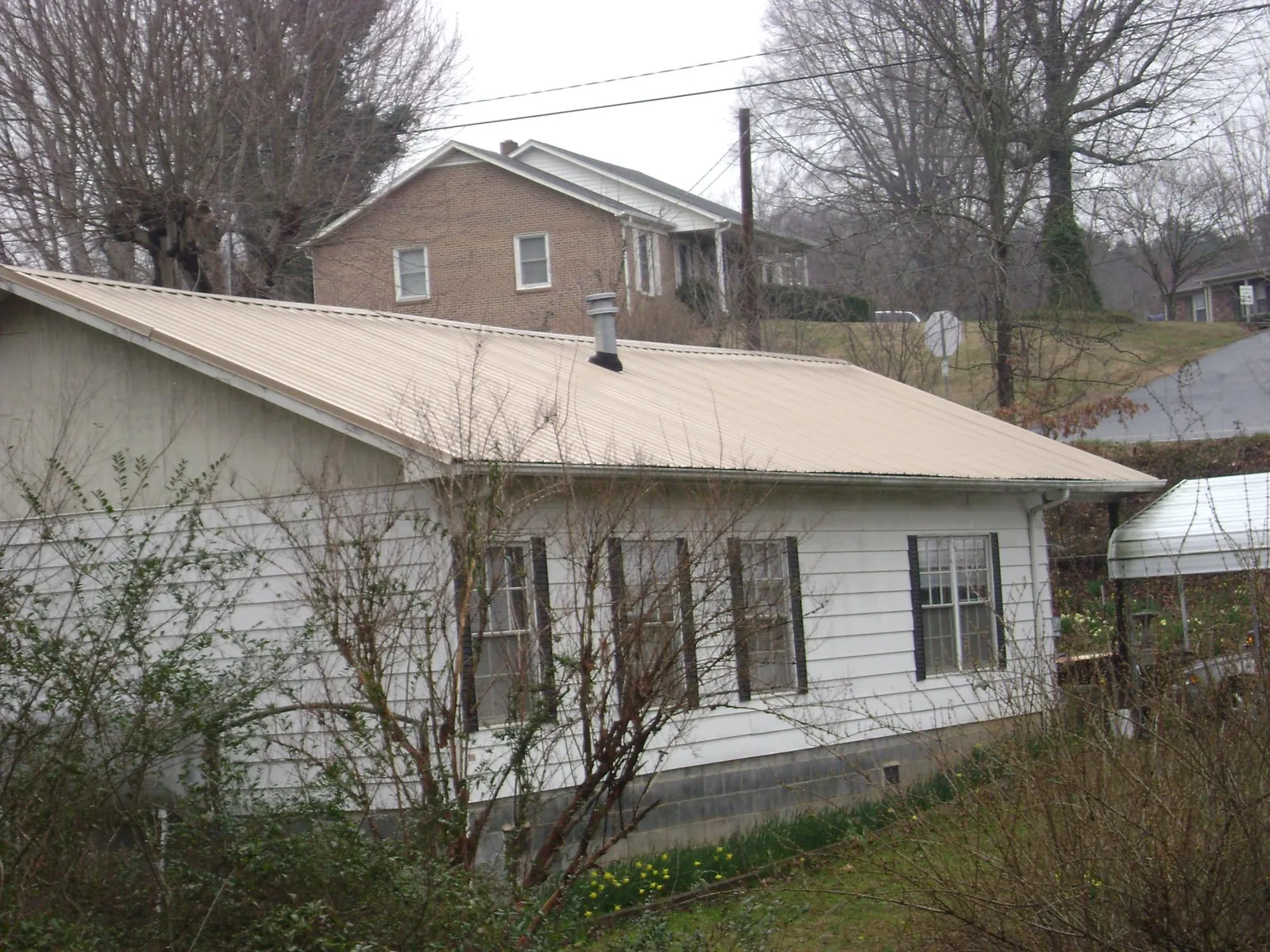 Tan metal roof on a white sided house set into a hillside — Commercial Roofing by Roofing Brothers in Luray